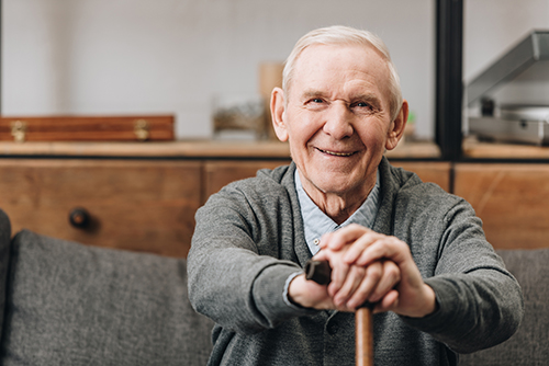 Elderly man sitting on a couch with his hands resting on his walking cane